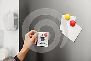 Woman putting paper sheet on refrigerator door at home