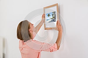 Woman Putting Photo Frame On Wall