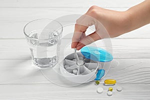 Woman putting pill into plastic box at white wooden table, closeup