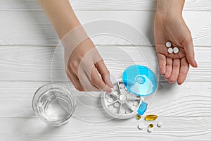 Woman putting pill into plastic box at white wooden table, top view