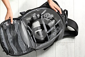 Woman putting professional photographer`s equipment into backpack on floor