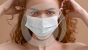 Woman Putting On Protective Face Mask Posing Over Beige Background