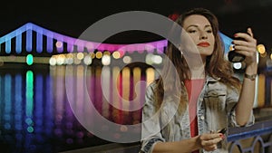 Woman Putting Red Lipstick Outside at Night City Lights Reflecting in the Water in Kiev