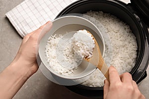 Woman putting rice into bowl from cooker in kitchen