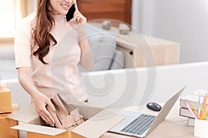 A woman putting shoes in a cardboard box, receiving orders from their phones and laptop computers, online sales from home. being a