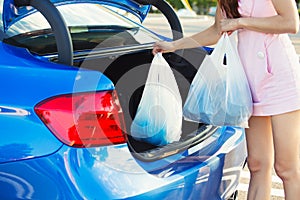 Woman putting shopping bags inside trunk of blue car