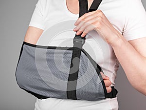 Woman putting on sling to support injured arm. Elbow, shoulder, forearm, wrist pain caused by trauma, injury, chronical