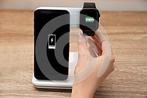 Woman putting smartwatch onto wireless charger at table, closeup. Modern workplace accessory