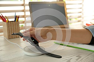 Woman putting smartwatch onto wireless charger at white wooden table, closeup. Modern workplace accessory