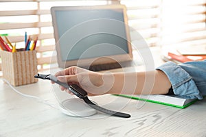 Woman putting smartwatch onto wireless charger at wooden table, closeup. Modern workplace accessory