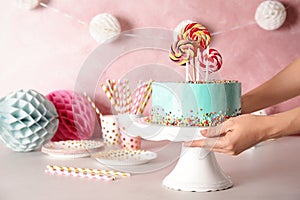 Woman putting stand with fresh delicious cake on against color background, closeup.