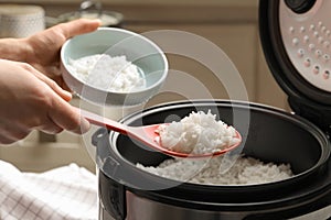 Woman putting tasty rice into bowl from cooker in kitchen