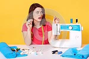 Woman putting thread in sewing machine, keeps hands up while sewing clothes at freelance work, brunette girl dressed casually.