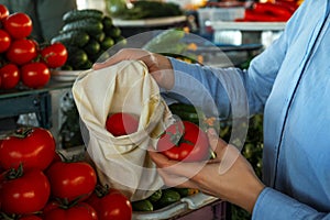 Woman putting tomato into cotton eco bag at wholesale market, closeup. Life without plastic