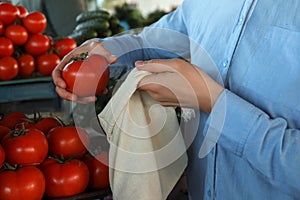 Woman putting tomato into cotton eco bag at wholesale market, closeup. Life without plastic