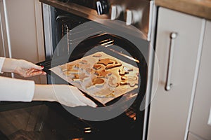 Woman putting tray with christmas cookies in oven close up in modern kitchen. Baking gingerbread cookies. Family holiday