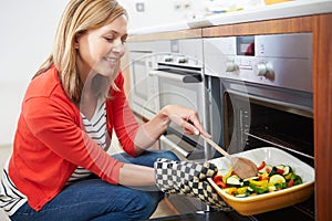 Woman Putting Tray Of Roast Vegetables Into Oven