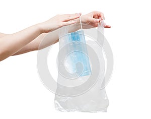 Woman is putting used disposal nonwoven safety mask in plastic bag before throwing it away.