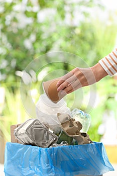 Woman putting used paper cup into trash bin on blurred background with space for text. Recycling problem