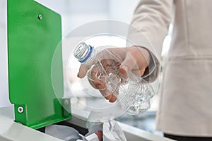 Woman putting used plastic bottle into trash bin in modern office. Waste recycling