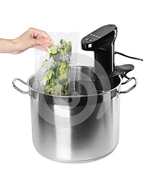 Woman putting vacuum packed broccoli into pot with sous vide cooker on white background, closeup. Thermal immersion circulator