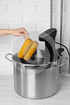 Woman putting vacuum packed corn into pot, closeup. Sous vide cooking