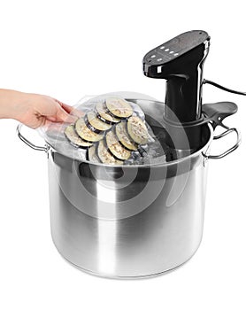 Woman putting vacuum packed eggplant into pot with sous vide cooker on white background, closeup. Thermal immersion circulator