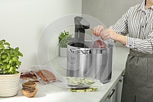 Woman putting vacuum packed meat into pot in kitchen, closeup. Thermal immersion circulator for sous vide cooking