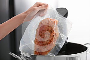 Woman putting vacuum packed meat into pot with sous vide cooker, closeup. Thermal immersion circulator