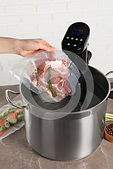 Woman putting vacuum packed meat into pot with sous vide cooker, closeup. Thermal immersion circulator