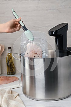 Woman putting vacuum packed meat into pot with sous vide cooker at table, closeup. Thermal immersion circulator