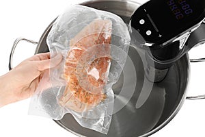 Woman putting vacuum packed meat into pot with sous vide cooker on white background, top view. Thermal immersion circulator