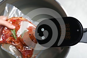 Woman putting vacuum packed meat into pot with thermal immersion circulator, closeup. Sous vide cooking