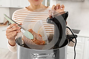 Woman putting vacuum packed meat into pot and using thermal immersion circulator, closeup. Sous vide cooking