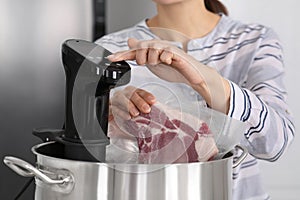 Woman putting vacuum packed meat into pot and using thermal immersion circulator, closeup. Sous vide cooking