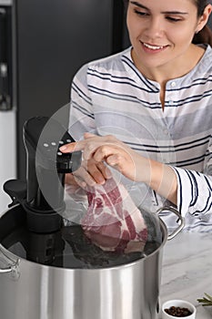 Woman putting vacuum packed meat into pot and using thermal immersion circulator. Sous vide cooking