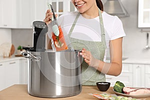Woman putting vacuum packed salmon into pot with sous vide cooker in kitchen, closeup. Thermal immersion circulator