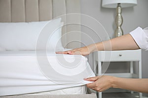 Woman putting white fitted sheet over mattress on bed indoors, closeup