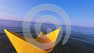 Woman putting yellow paper boat on surface of water of sea waves close-up.