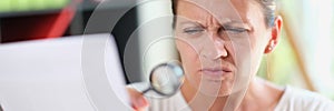 Woman with puzzled face reads document or recipe with magnifying glass in her hand.