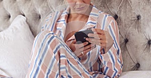 Woman In Pyjamas Sitting On Bed With Mobile Phone Checking Messages