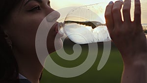 Woman quenches her thirst in a field at sunset. Silhouette of a girl drinks water from a plastic bottle, sun rays