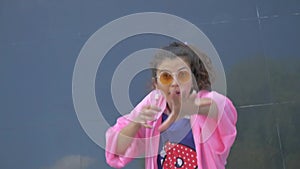 A woman in a quirky pink outfit joyfully dancing in front of a building. Vibrant woman in pink ensemble showing off dance moves