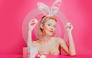 Woman with rabbit ears hold easter egg over pink background.