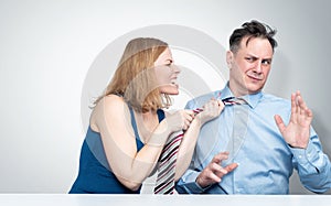 The woman in a rage grabbed the man by the tie and screams at him, the man covers himself with his hands and looks scared