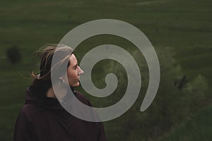 Woman in a rain anorak stands on the hill, deep green background.