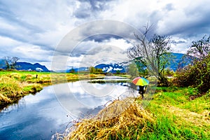 Woman with a rainbow colored Umbrella under dark rain clouds on a cold spring day at the lagoons of Pitt-Addington Marsh