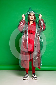 Woman in raincoat standing in studio on green background