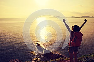 Woman with raised hands standing at seaside mountain