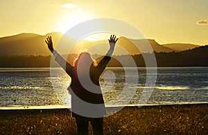 Woman raising hands worshiping praising praying God beautiful sunset